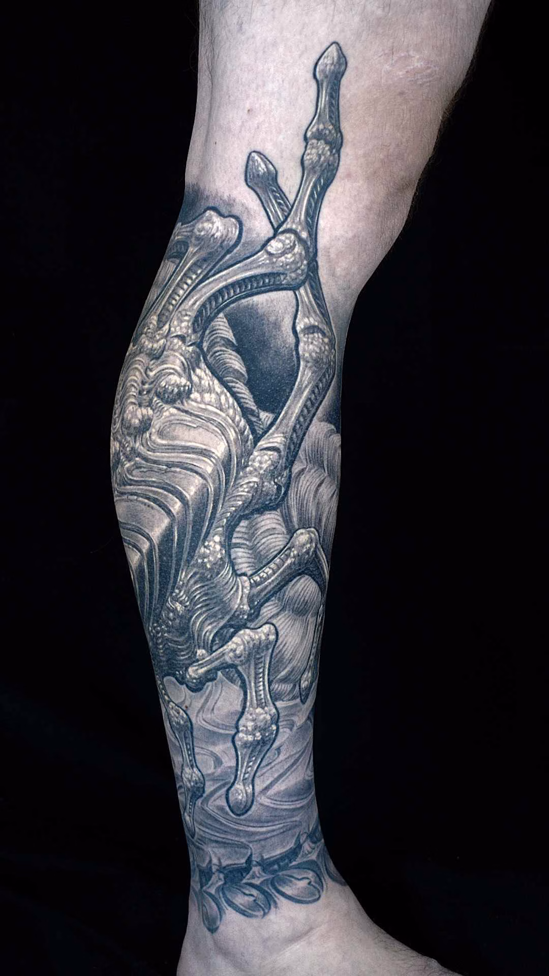 Schräg-frontale Perspektive des Tattoos: Feine organisch-mechanische Texturen der Facehugger-Gliedmaßen im Verlauf über das Schienbein bis zum Knöchelansatz