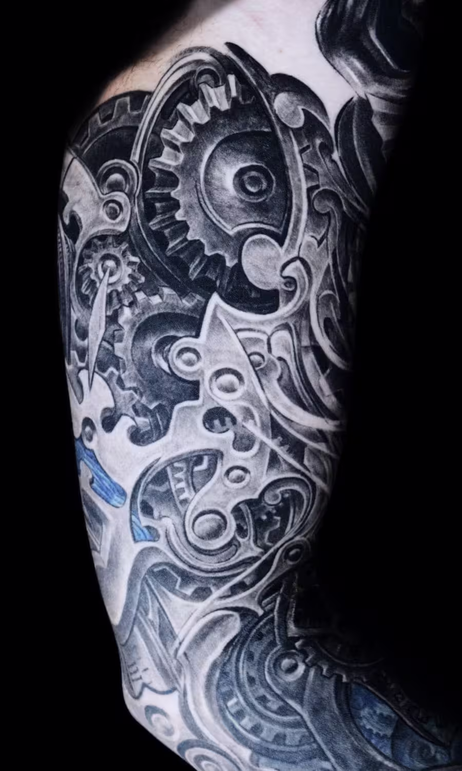 Biomechanik-Tattoo im H.R. Giger Stil, das fließend in ein mechanisches Uhrwerk-Design übergeht, gestochen von Raul bei Hits for Life Tattoo München