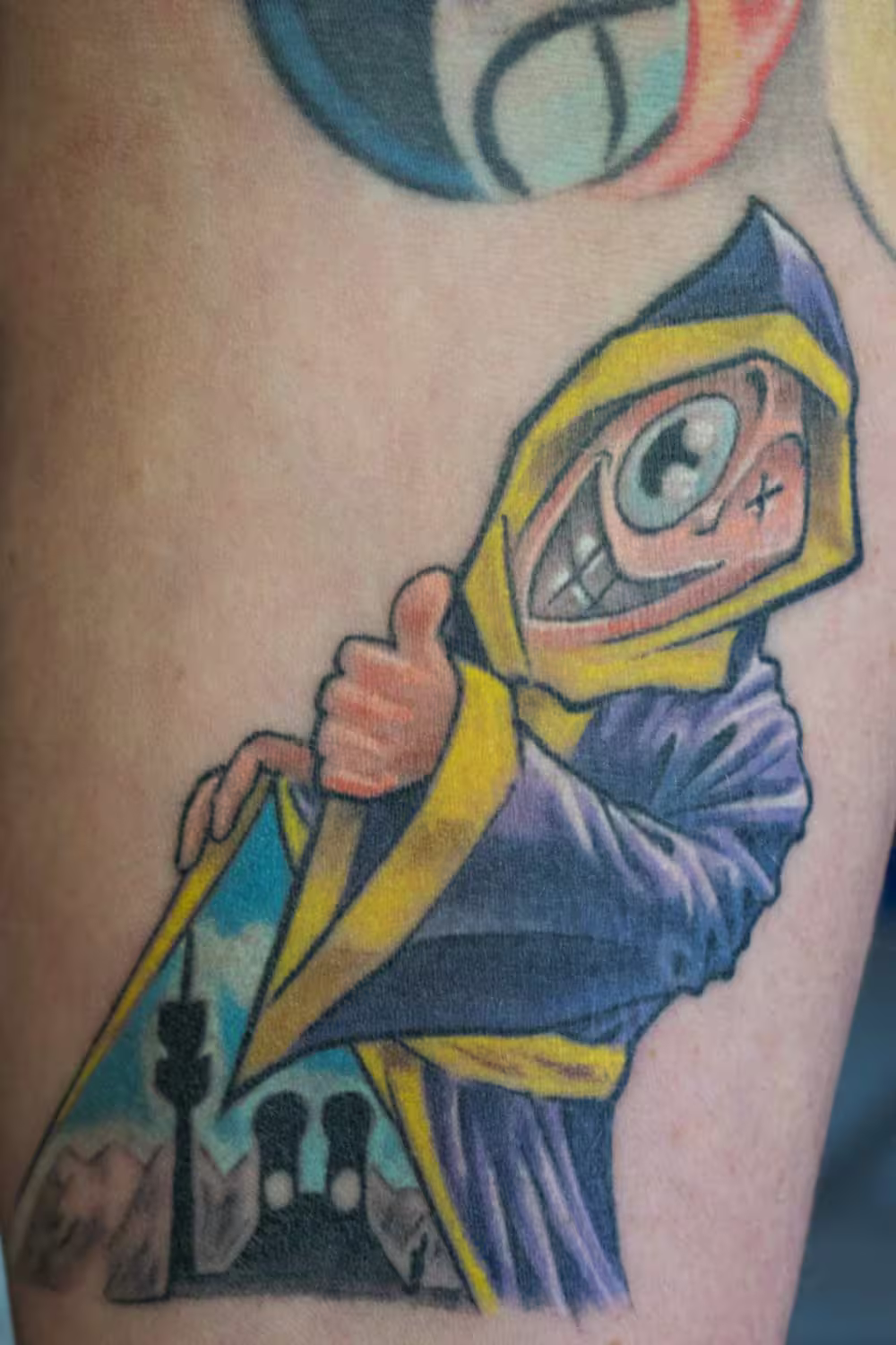 Münchener Kindl Tattoo im Comic-Stil mit Thumbs-up-Geste und der Münchener Skyline innerhalb der hochgezogenen Kutte, kreatives Design von Raul bei Hits for Life