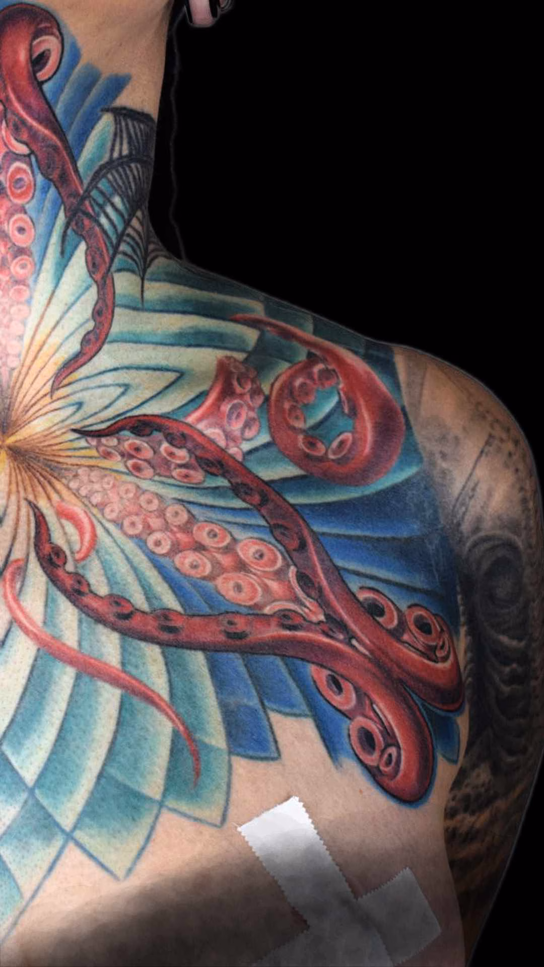 Ste Brust tentakel Mandala Tattoo, Frontales Chest- und Hals-Tattoo im Raum München: Ein blau-türkises Mandala in Dreiecksform, das die Kurven des Dekolletés nutzt, kombiniert mit roten Tentakeln als stilisierte Staubblätter, Integration bestehender Tattoos am Hals, frontal linke Seite
