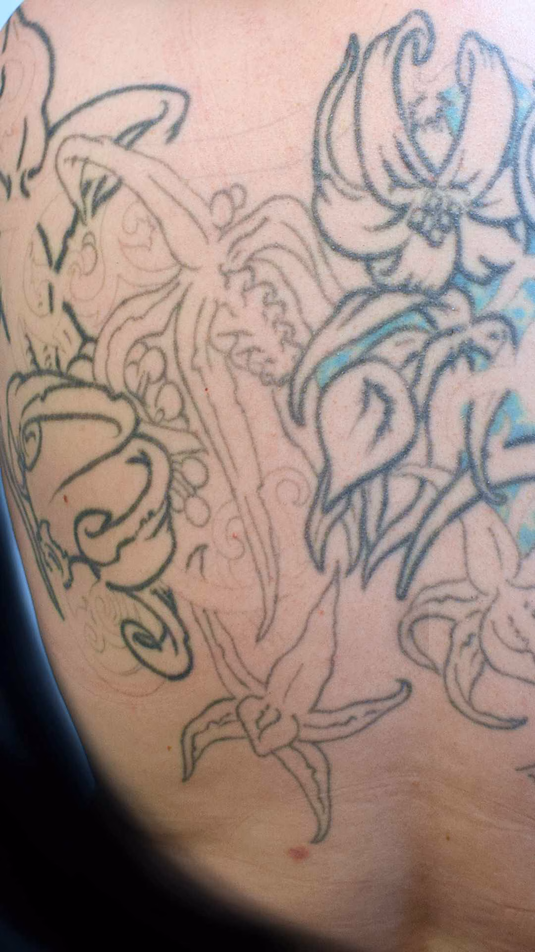 Detailaufnahme des Grinsekatze Tattoos: Filigranes Stippling und Pepper-Shading lockern das Blumenbukett auf, kombiniert mit einer pinken Kannenblume