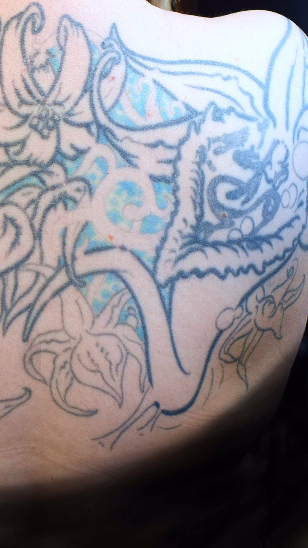 Buntes Grinsekatze Tattoo auf der Schulter als komplexes Cover-up. Das Alice im Wunderland Motiv nutzt Türkis, Lila und Pepper-Shading zur Überdeckung alter Tätowierungen