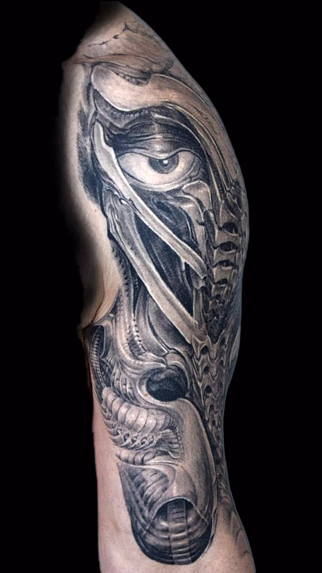 Template 1920 1080 mit Filtern Frontale Studioaufnahme des Knochengesicht-Tattoos am Oberarm über dem Bizeps bis zur Ellbeuge. Sichtbar sind die breiten, maskulinen Querrippen der insektoiden Maske und der haubenartige Abschluss auf dem Bizepsmuskel im tiefen Black-and-Grey-Stil