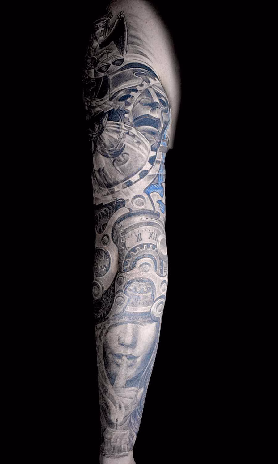 Biomechanik Uhr Frau mit Finger vor den Lippen zum Zeichen still Tattoo-Übergang von den feinen Gesichtszügen zu den wuchtigen Zahnrädern und Exoskeletten des biomechanischen Ellbogens und Stundenglas sowie Maske am Oberarm
