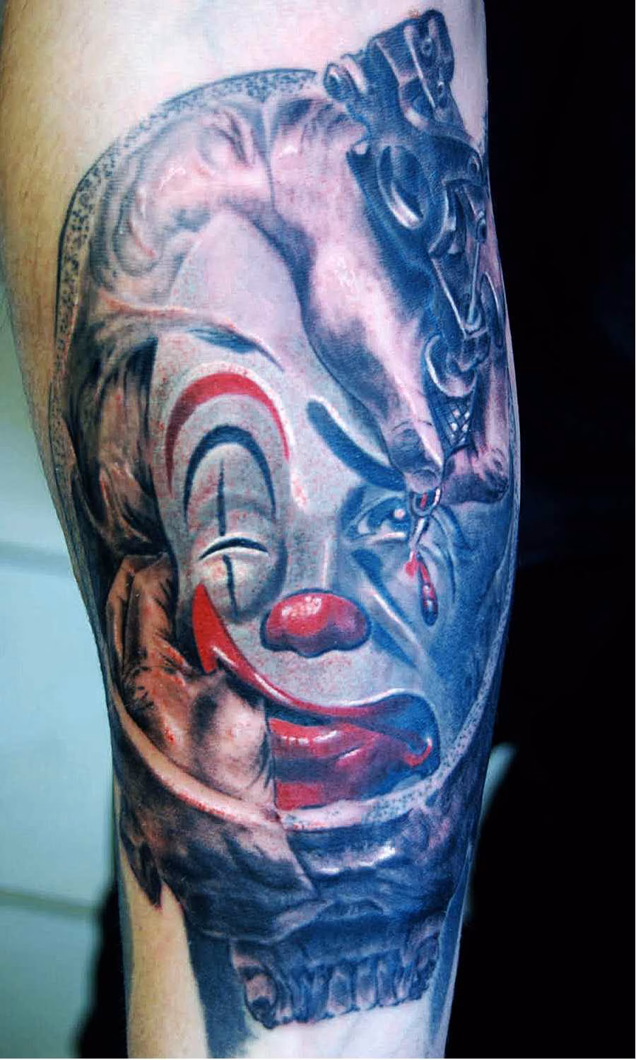 Rene-Clown-Tattoo Clown-Tränen Tattoo, Aufnahme frisch gestochen eines detailreichen Black-and-Grey-Tattoos auf der Innenseite eines männlichen Unterarms. Zu sehen ist ein surrealistisches Clownsgesicht, dessen Mimik zwischen Traurigkeit und erzwungener Fröhlichkeit schwankt: Eingebettet in die fossa cranii media, den Innenbereich eines von hinten und oben zu sehenden Totenschädels übernimmt das Clownsgesicht Schädel-Innen-Strukturen wie die ala minor ossis sphenoidalis für die Augenbrauen , ein Daumen drückt den Mundwinkel in der Wange nach oben, während eine tätowierte Hand im Stil von M. C. Escher dem Clown mit einer Tätowiermaschine eine Träne unter das Auge zeichnet