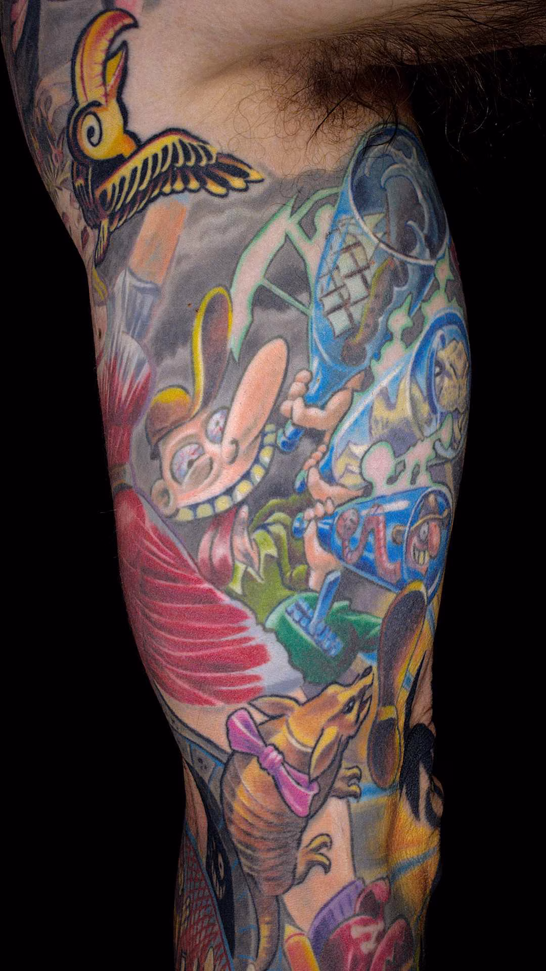 Flucht aus Berlin Tattoo Sleeve Wimmelbild Nietsche Historia in Buntes Comic Tattoo nach Gerhard Seyfried am inneren Bizeps mit lachendem Säufer, Flaschen und Gürteltier – Custom Tattoo München